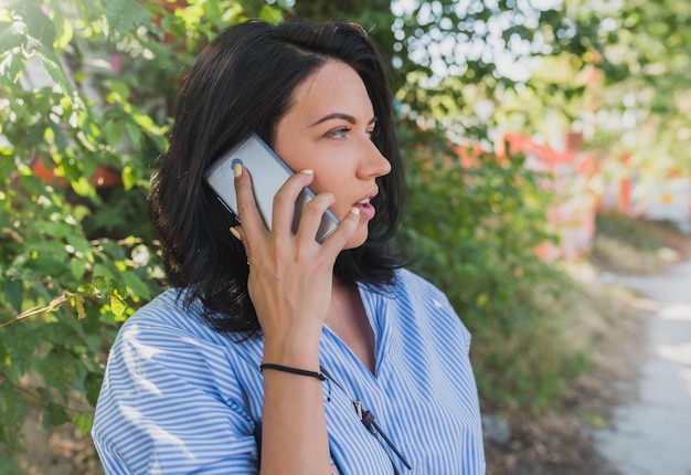 Zdjęcie wesoła młoda kaukaska kobieta ubrana w niebieską koszulę rozmawia przez telefon komórkowy o nowym projekcie ludzie styl życia i koncepcja biznesowa