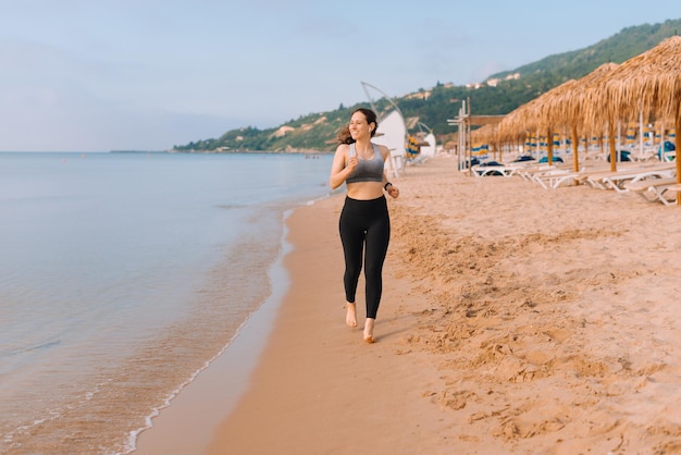 Wesoła młoda kobieta biegająca po plaży podczas słuchania muzyki