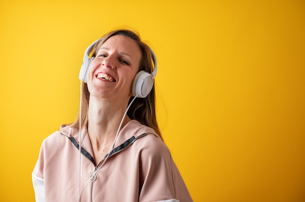 Wesoła młoda kobieta śmieje się radośnie, słuchając muzyki w słuchawkach na głowie.