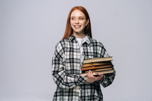 Wesoła młoda kobieta studentka trzymająca książki i odwracająca wzrok na odosobnionym tle