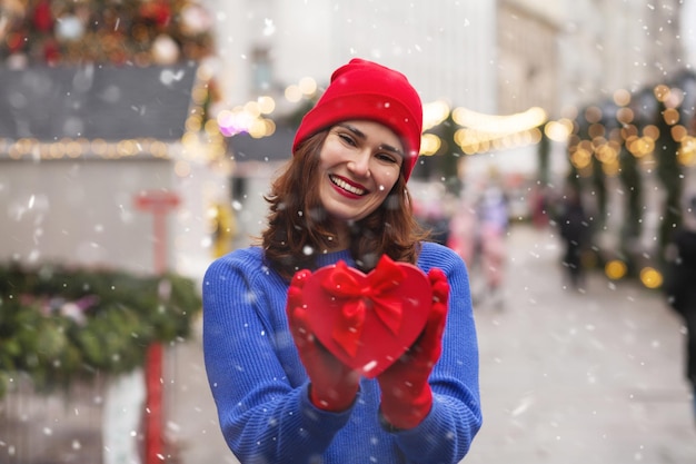 Wesoła młoda kobieta trzyma pudełko z wstążką na jarmarku bożonarodzeniowym. Pusta przestrzeń