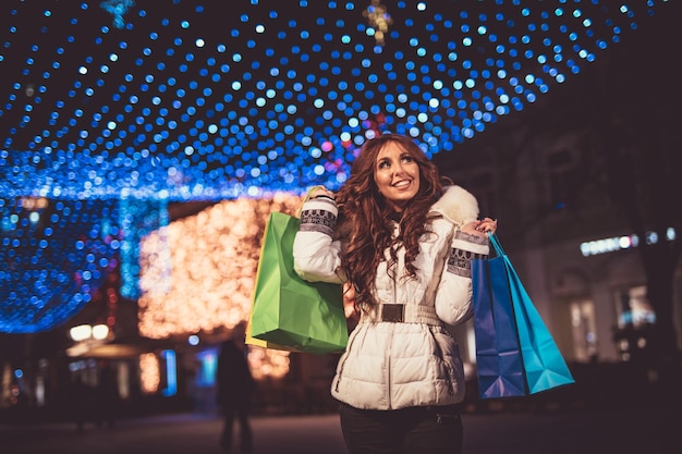 Wesoła młoda kobieta z kolorowymi torbami na zakupy zabawy na ulicy miasta w czasie świąt Bożego Narodzenia.