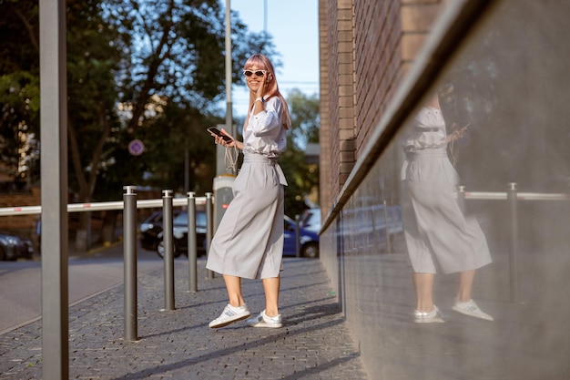 Wesoła młoda kobieta ze smartfonem stojąca na ulicy