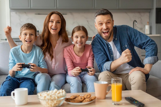 Wesoła młoda rodzina z dwoma dziećmi grającymi w gry wideo w domu