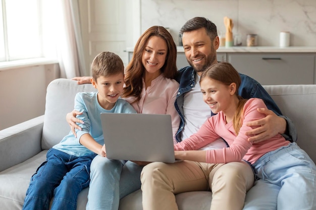 Wesoła młoda rodzina z dziećmi bawiąca się laptopem w domu