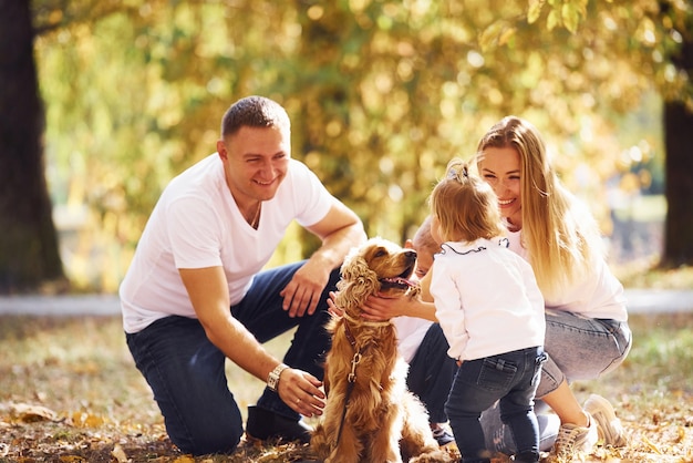 Wesoła młoda rodzina z psem odpoczywa razem w jesiennym parku.