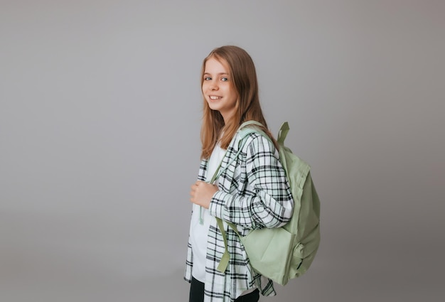 Zdjęcie wesoła nastolatka 111213 lat w mundurku szkolnym nosi plecak na szarym tle mody szkolnej