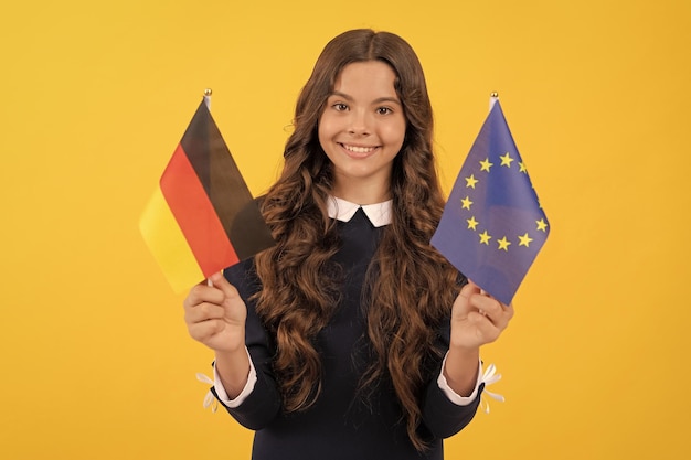 Wesoła nastolatka trzyma unię europejską i niemiecką flagę na żółtym tle podróży