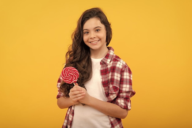 Wesoła nastolatka z długimi włosami trzyma lizak karmelowy cukierek na żółtym tle sklep z karmelami