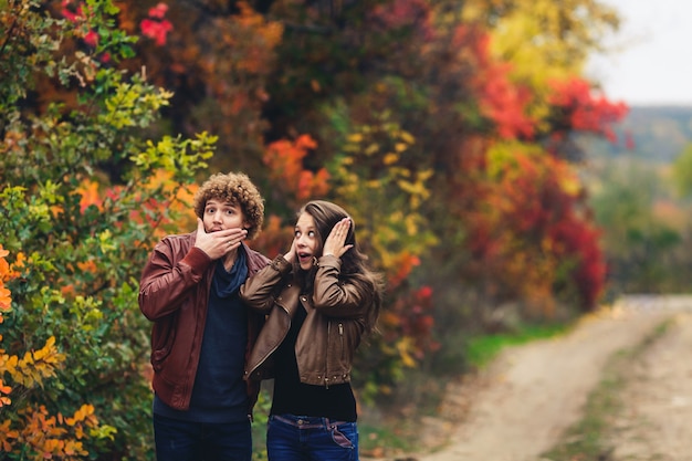 Wesoła para pokazuje emocje. mężczyzna i kobieta w skórzanych kurtkach i dżinsach pokazują zdziwienie na tle jesiennych drzew.