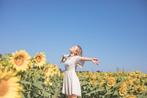Wesoła pozytywna młoda kobieta pozuje na aparacie wśród pól słoneczników Szczęśliwa dziewczyna