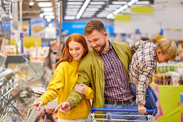 Wesoła Rodzina Z Niespokojnym Zabawnym Synem W Supermarkecie, Mężczyzna I Kobieta Wybierający Jedzenie W Sklepie, Mężczyzna Trzyma Szalonego Chłopca W Rękach