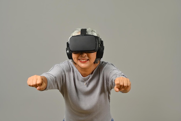 Wesoła starsza kobieta w okularach wirtualnej rzeczywistości symulująca jazdę samochodem w okularach VR izolowana na białym tle