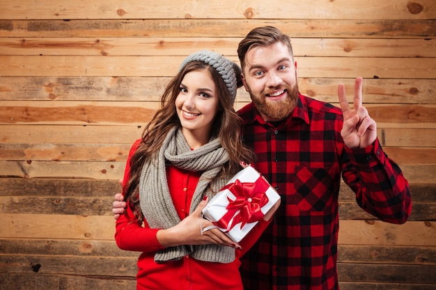 Wesoła szczęśliwa para w zimie nosi stojąc i trzymając pudełko na białym tle na drewnianej ścianie