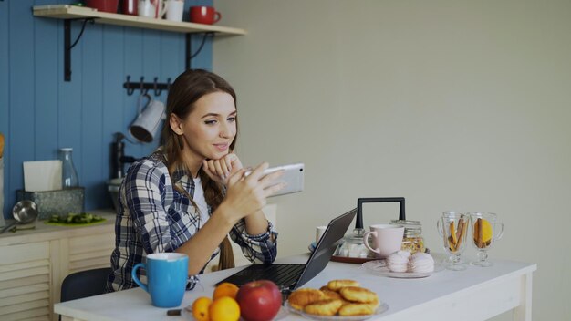 Wesoła uśmiechnięta kobieta rozmawiająca na czacie wideo online za pomocą smartfona w kuchni w domu