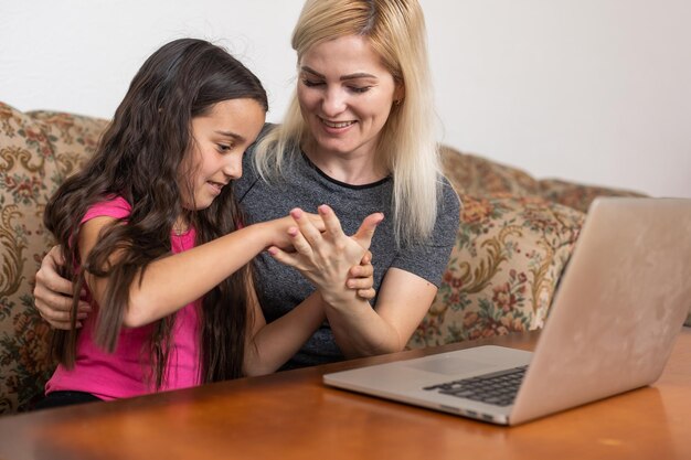 Wesoła, uśmiechnięta, szczęśliwa matka i jej mała ciekawa córka leżą na podłodze w domu i używają laptopa do oglądania kreskówek, dziewczyna wskazuje na monitorze w weekend.
