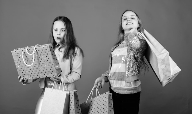 wesołe dzieci Małe dziewczynki siostry Oszczędności sióstr i rodziny na zakupach Moda dziecięca Niebieskie tło Wyprzedaże i rabaty Małe dziewczynki z torbami na zakupy małe siostry w sklepie