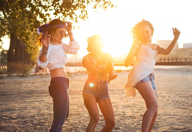 Wesołe przyjaciółki tańczące na plaży podczas zachodu słońca