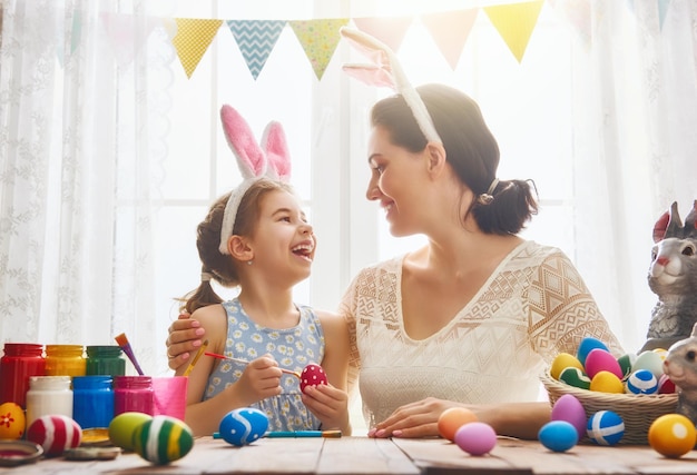 Wesołego Alleluja! Matka i jej córka malują pisanki. Szczęśliwa rodzina przygotowuje się do Wielkanocy. Cute dziewczynka dziecko sobie uszy królika na Wielkanoc.