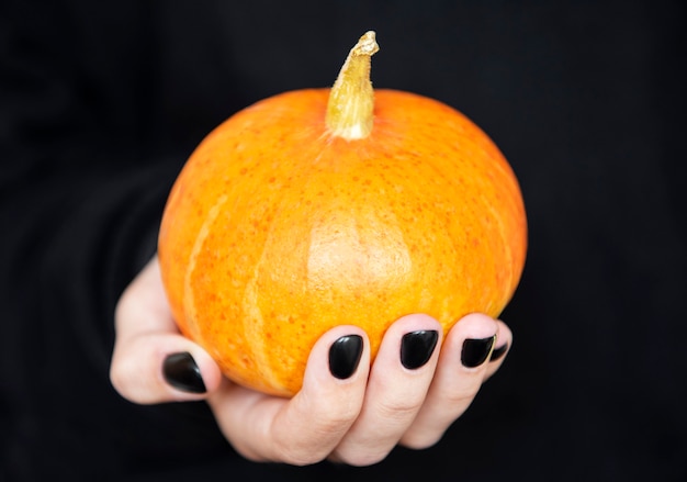 Wesołego Halloween. Kobiece ręce trzymając śmieszne dynie na czarnym tle. Manicure z czarnym lakierem do paznokci