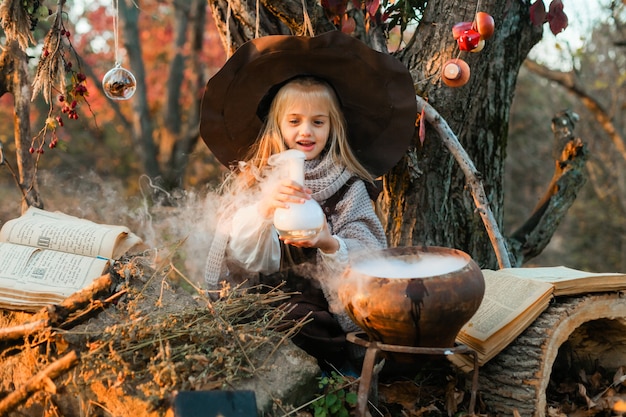 Wesołego Halloween. Słodka dziewczyna w stroju wiedźmy jest w jaskini wiedźmy. Śliczna wesoła mała wiedźma warzy magiczną miksturę. Halloween.