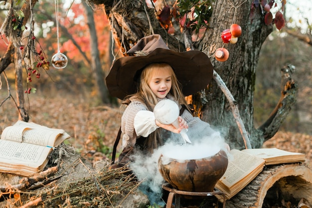 Wesołego Halloween. Słodka Dziewczyna W Stroju Wiedźmy Jest W Jaskini Wiedźmy. śliczna Wesoła Mała Wiedźma Warzy Magiczną Miksturę. Halloween.