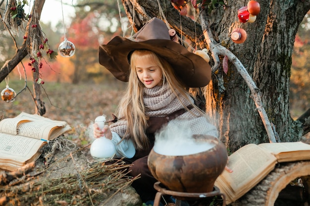 Wesołego Halloween. Słodka dziewczyna w stroju wiedźmy jest w jaskini wiedźmy. Śliczna wesoła mała wiedźma warzy magiczną miksturę. Halloween.