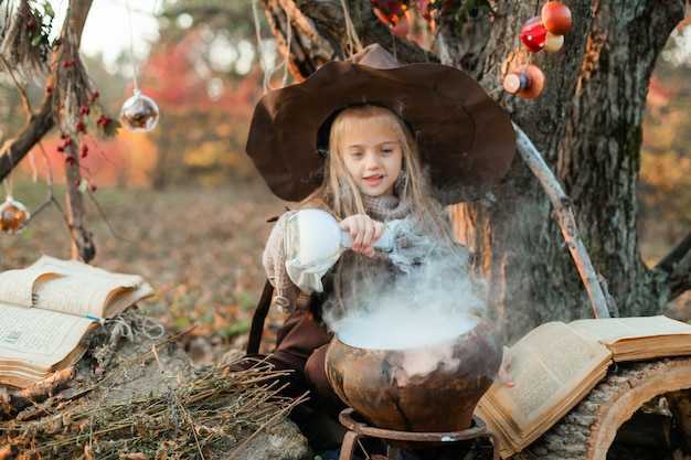 Wesołego Halloween. Słodka dziewczyna w stroju wiedźmy jest w jaskini wiedźmy. Śliczna wesoła mała wiedźma warzy magiczną miksturę. Halloween.