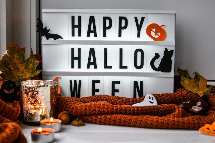 Zdjęcie wesołego halloween. tekst w białym podświetlanym pudełku, na tle swetra, suszonych liści halloween jesienna dekoracja na parapecie. deszczowe okno. światło bokeh. duch, nietoperz dyniowy, czarny kot.