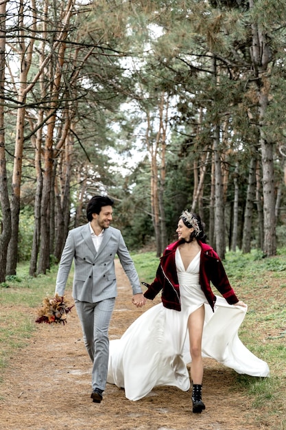 Wesoli i szczęśliwi nowożeńcy biegają trzymając się za ręce i uśmiechając się na zdjęciach wysokiej jakości
