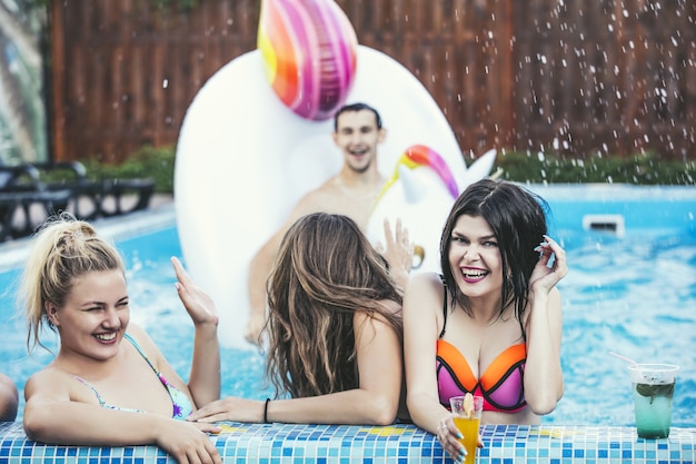Wesoli młodzi przyjaciele w basenie na koktajlu z nadmuchiwanym jednorożcem