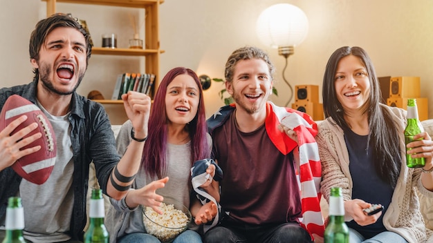 Wesoło podekscytowani czterej przyjaciele oglądają futbol amerykański w telewizji w domu