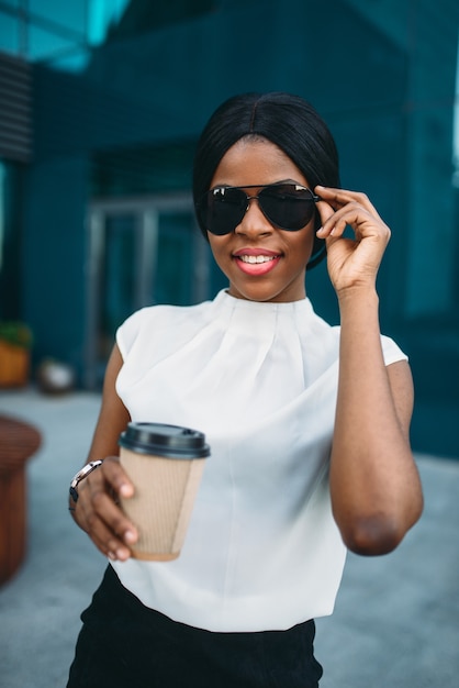 Wesoły biznes kobieta w okularach przeciwsłonecznych z tekturową filiżanką kawy odpoczynek podczas przerwy na świeżym powietrzu