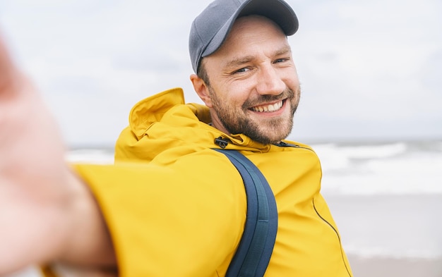 wesoły brodaty młody człowiek podróżujący samotnie biorący selfie na plaży - Koncepcja przygody wanderlust na plaży