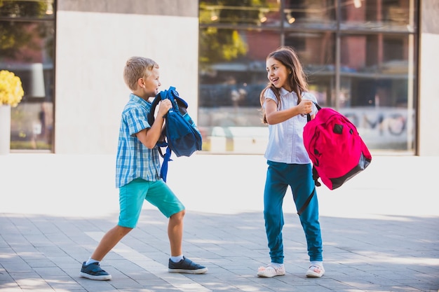 Wesoły chłopak i dziewczyna robiący fałszywy plecak walczą na zewnątrz w pobliżu szkoły Aktywne spędzanie wolnego czasu Gry, aby pozbyć się negatywnych emocji