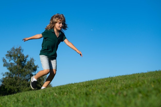 Wesoły chłopiec biegający po zielonej trawie szczęśliwe dziecko bawiące się w zielonym wiosennym polu na tle nieba