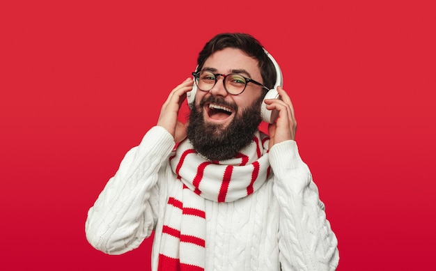Wesoły człowiek w zimowym swetrze i szaliku słuchając muzyki w słuchawkach