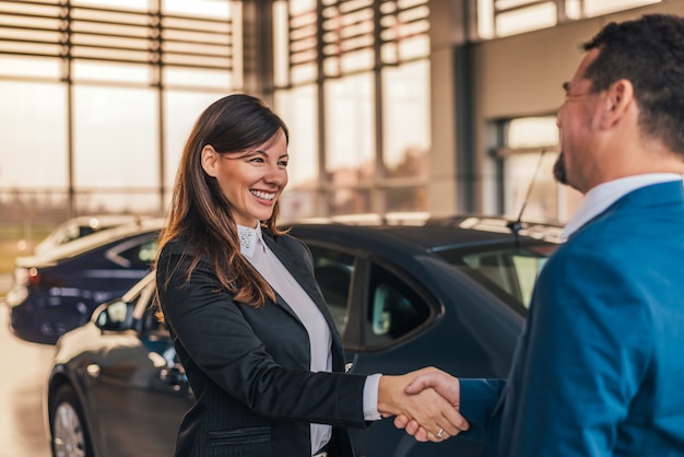 Wesoły dealer samochodowy uścisk dłoni z klientem w salonie.