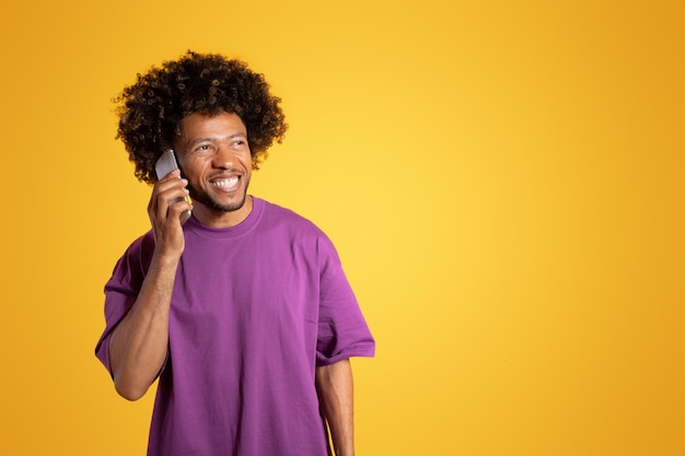 Wesoły, dojrzały, czarny, kędzierzawy mężczyzna w fioletowej koszulce rozmawia przez smartfona i patrzy na wolne miejsce