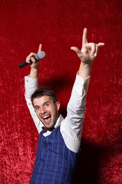 Wesoły ekscentryczny showman z mikrofonem pokazujący rockowy gest i bawiący się podczas występu