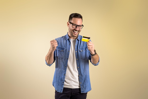 Wesoły klient płci męskiej patrzący na kartę kredytową i pompujący pięść po otrzymaniu nagrody online