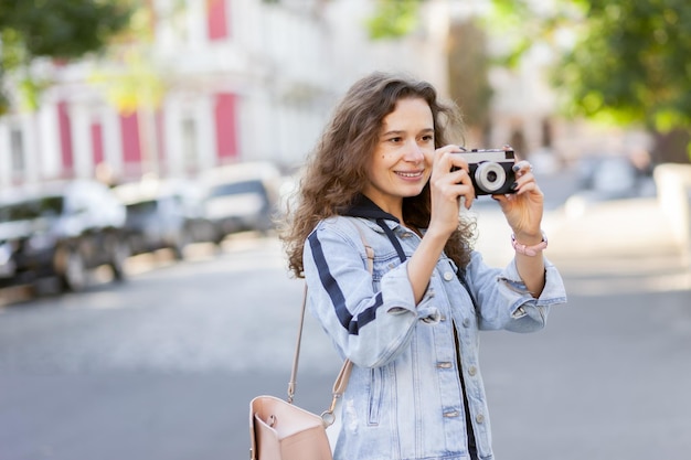 Wesoły kręcony włos kobieta turysta z retro aparatem spacerującym wzdłuż miasta w jasny słoneczny dzień Koncepcja podróży