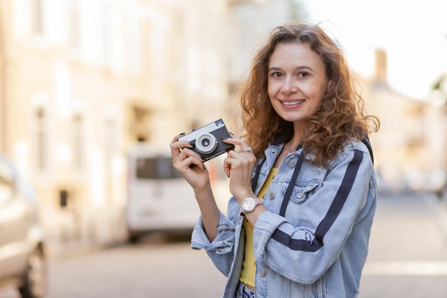 Wesoły Kręcony Włos Kobieta Turysta Z Retro Aparatem Spacerującym Wzdłuż Ulicy Miasta W Jasny Słoneczny Dzień Koncepcja Podróży