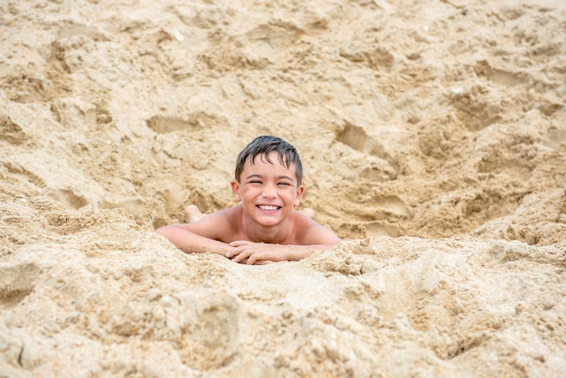 Wesoły mały chłopiec brunetka na plaży bawi się piaskiem koncepcja podróży dla dzieci Wakacje na morzu