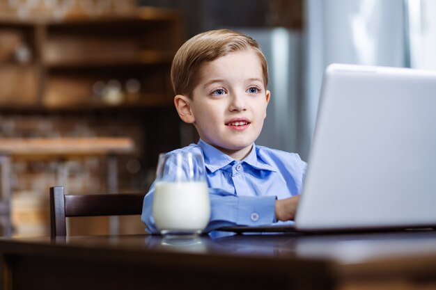 Wesoły mały chłopiec za pomocą swojego laptopa podczas odpoczynku w kuchni