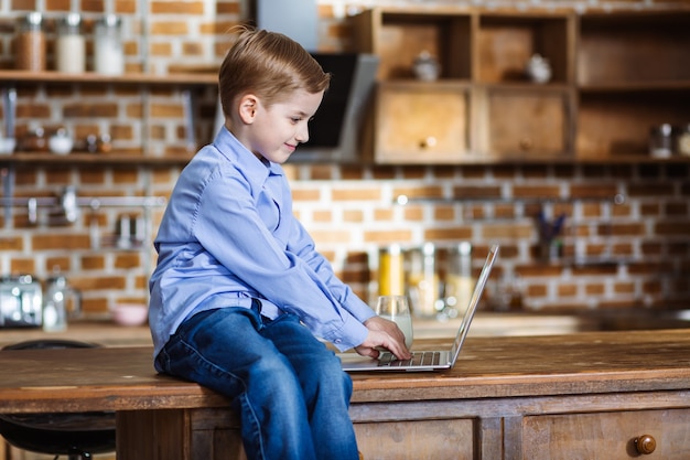 Wesoły mały chłopiec za pomocą swojego laptopa siedząc na stole