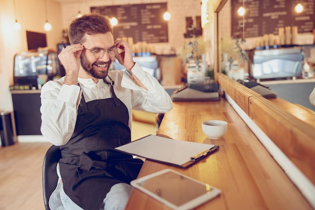 Wesoły męski barista zakładający okulary w kawiarni