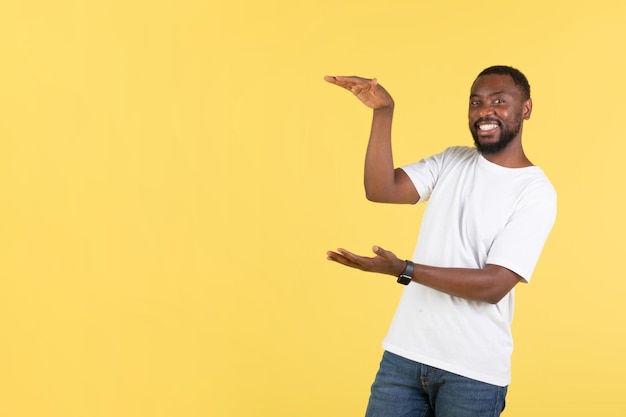 Wesoły mężczyzna afroamerykański pokazujący niewidoczny produkt na żółtym tle
