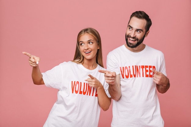wesoły mężczyzna i kobieta ochotnicy noszący jednolite koszulki wskazujące palce na bok na białym tle