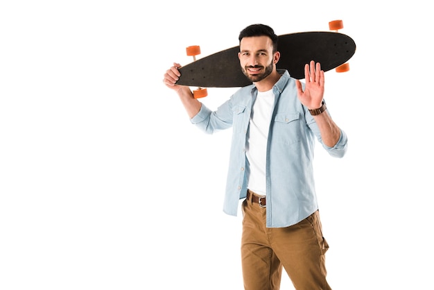 Wesoły mężczyzna z longboardem patrzący w kamerę i pokazujący gest powitania na białym tle